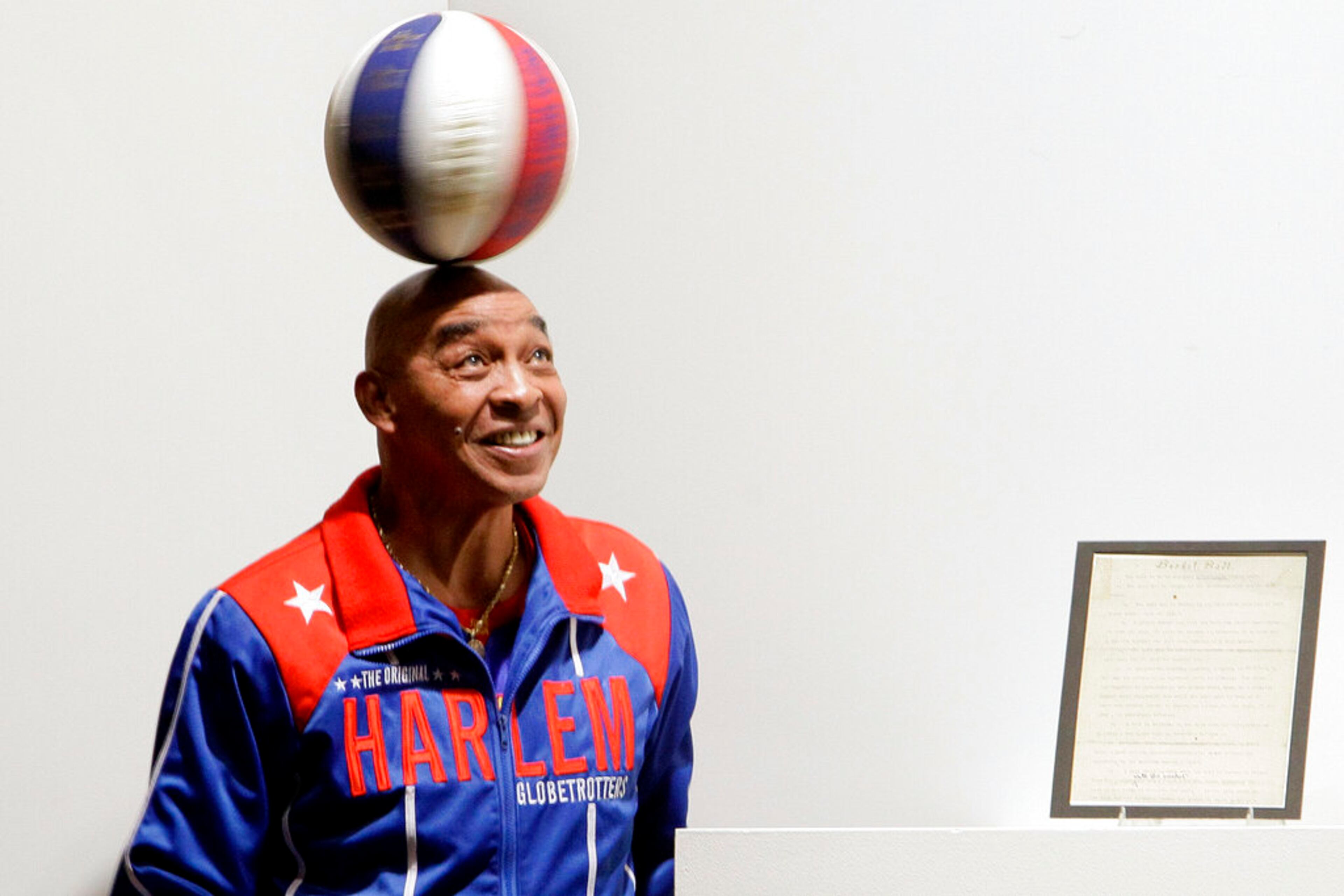 FILE - In this Dec. 10, 2010, file photo, Harlem Globetrotters Fred "Curly" Neal spins a ball on his head prior to the bidding for the Naismith Rules, the original rules for basketball, framed at right, at Sotheby's in New York. Neal, the dribbling wizard who entertained millions with the Harlem Globetrotters for parts of three decades, has died the Globetrotters announced Thursday, March 26, 2020. (AP Photo/Richard Drew, File)